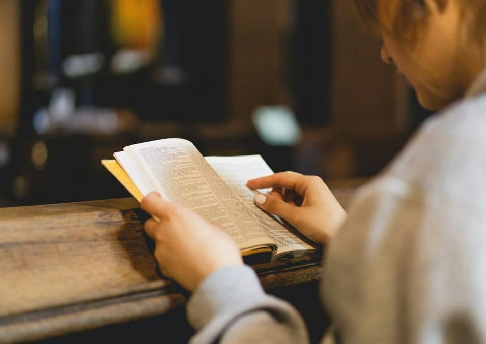 A person reading a Bible at a church pew.
